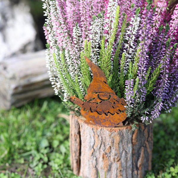 Gartendekoration Wichtel aus Edelrost in einem Pflanzgefäß aus Baumstamm mit Heidekrautpflanzen