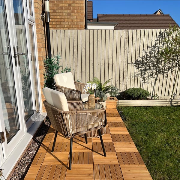 Garten-Lounge-Set auf einer Holzterrasse mit zwei Sesseln, Sitzkissen, Beistelltisch und Holzfliesen neben einer Rasenfläche.