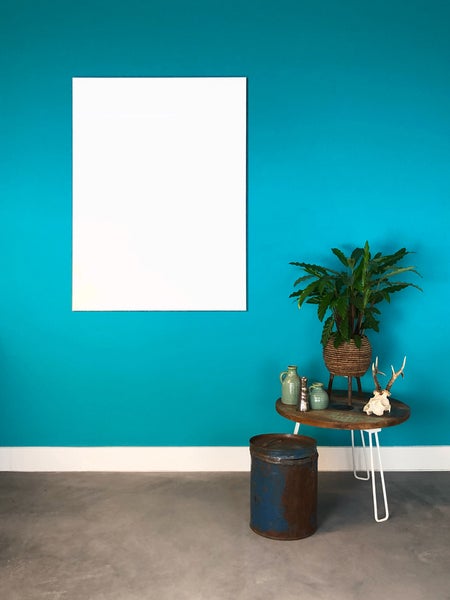 Weiße Infrarotheizung an einer türkisfarbenen Wand neben einem Beistelltisch mit Zimmerpflanze auf grauem Boden.