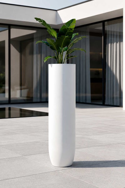 Hoher, weißer zylindrischer Pflanzkübel mit grüner Pflanze auf einer modernen Terrasse mit grauen Bodenplatten.