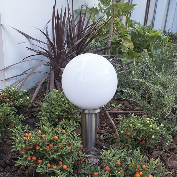 Kugelleuchte für den Außenbereich mit weißem Schirm und Edelstahl-Standfuß in einem Gartenbeet zwischen Pflanzen.