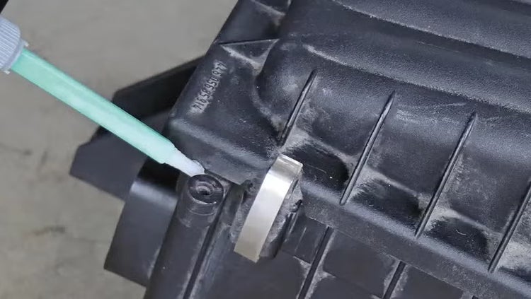 Eine Dosierdüse appliziert Klebstoff auf ein Kunststoffteil eines Luftfiltergehäuses.