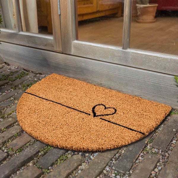Halbrunde Fußmatte aus Kokosfaser mit Herzmotiv vor einer Tür.