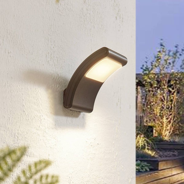 Moderne, gebogene LED-Außenwandleuchte in Dunkelbraun an einer Hauswand mit warmweißem Lichtschein.
