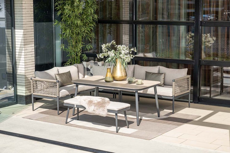 Modernes Garten-Lounge-Set aus Metall mit Ecksofa, gepolsterter Sitzbank und einem Esstisch auf einer hellen, organisierten Terrasse.