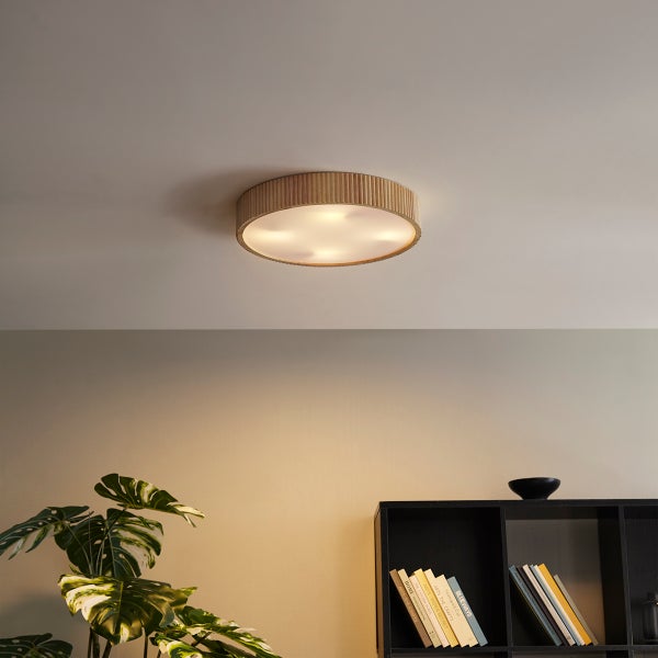 Moderne runde Deckenleuchte mit geriffeltem Holzrand in einem hellen Wohnraum mit schwarzem Regal und Monstera-Pflanze.