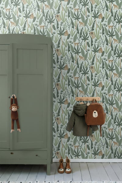 Organisiertes Kinderzimmer mit Vliestapete im Dschungel-Design mit Affenmotiven, grünem Holzschrank und Wandgarderobe mit Bärenrucksack.
