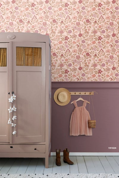 Florale Vliestapete kombiniert mit Wandpaneelen in einem hellen Zimmer mit Vintage-Schrank und Kinderkleidung an einer Hakenleiste.