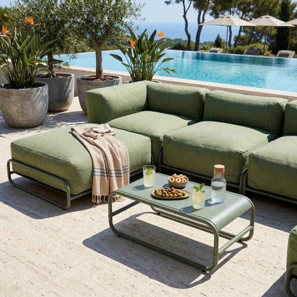 Modulare Gartenlounge mit grünen Polstern, passendem Couchtisch und Hocker an einem Pool auf einer hellen Terrasse.