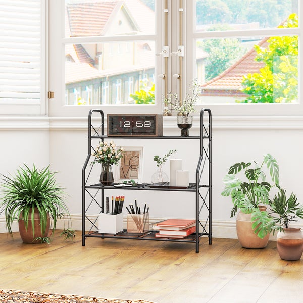 Schwarzes Metallregal mit drei Ebenen in einem hellen Raum vor einem Fenster, dekoriert mit Wohnaccessoires und umgeben von grünen Zimmerpflanzen.
