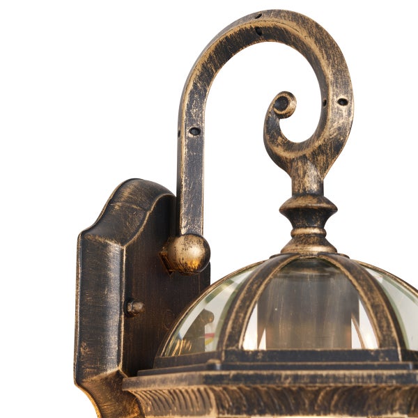 Detailansicht einer antiken Außenwandleuchte aus Metall in Schwarz und Gold mit Glasgehäuse und dekorativem geschwungenem Element.