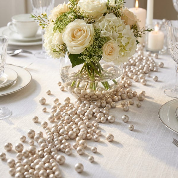 Festlich gedeckter Tisch mit einem Blumenstrauß in einer Glasvase und verstreuten Dekoperlen als Tischschmuck.