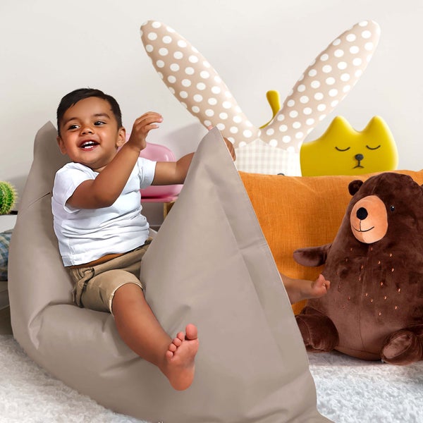 Ein Kind sitzt in einem grauen Sitzsack, umgeben von einem Bärenkuscheltier, einem Hasenkissen und einem gelben Katzenkissen.