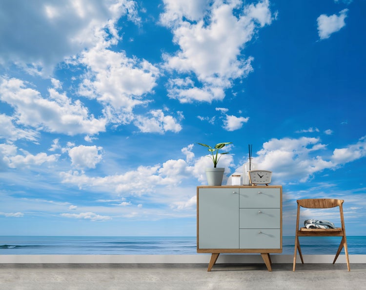 Szene mit Kommode, Dekoration und Stuhl vor einer Fototapete mit Himmel- und Meermotiv.