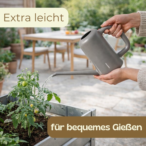 Person gießt eine Tomatenpflanze in einem Metall-Hochbeet mit einer leichten Gießkanne auf einer hellen Terrasse.