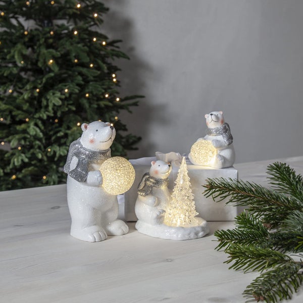 Dekorative Szene mit drei Eisbärenfiguren mit Schals, die leuchtende Kugeln und einen Weihnachtsbaum halten.