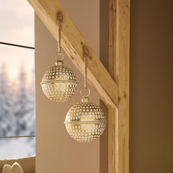 Zwei dekorative Hängekugeln mit Lochmuster an Juteschnüren hängend an einem Holzbalken für die weihnachtliche Innendekoration.