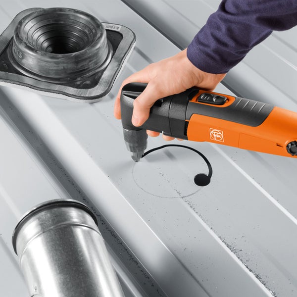 Fein Akku-Blechnibbler schneidet eine kreisförmige Öffnung in ein silbernes Trapezblech an einer Wand in einem hellen Gang.