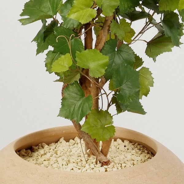 Künstlicher Weinstock mit grünen Blättern in einem runden Topf mit hellem Zierkies.