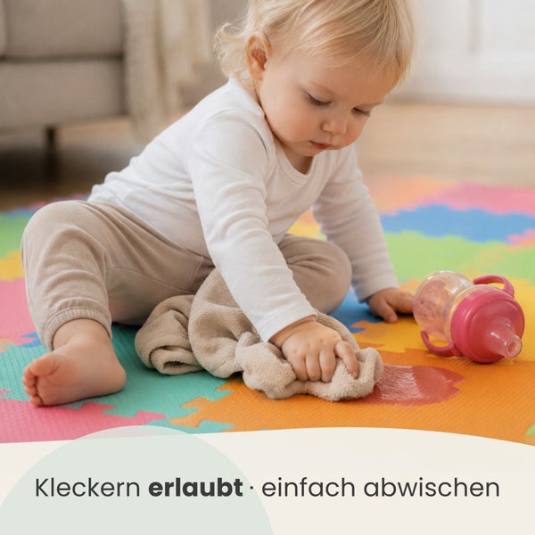 Kleinkind wischt verschüttete Flüssigkeit mit einem Tuch von einer abwischbaren Spielmatte aus Schaumstoff für Kinder.