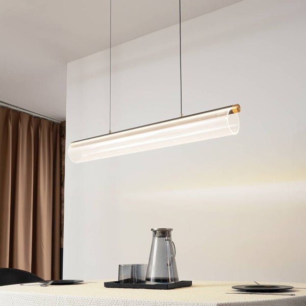 Moderne LED-Pendelleuchte in horizontaler Zylinderform aus Acryl mit Gold-Akzenten, hängend über einem hellen Esstisch in einem modernen Ambiente.