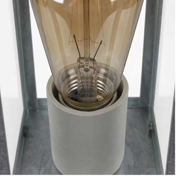 Nahaufnahme einer Vintage-Glühbirne in einer grauen Betonfassung, umgeben von einem grauen Metallrahmen.