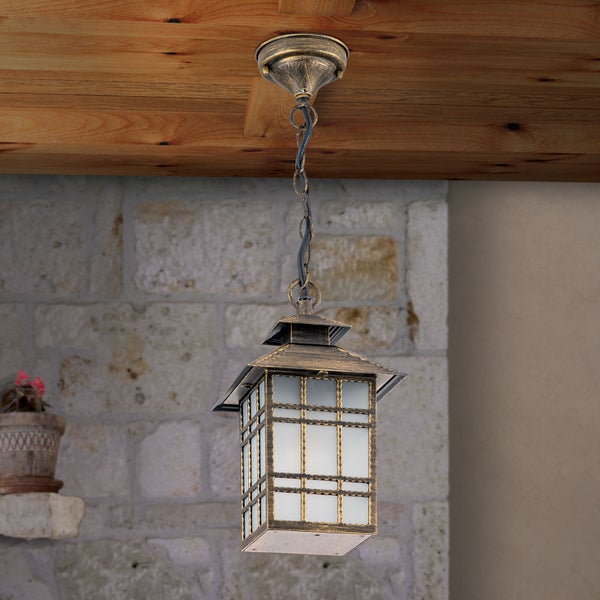 Rustikale Außenhängeleuchte in Laternenform mit Metallgitter und Glaseinsätzen, hängend an einer Holzdecke vor einer Steinwand.