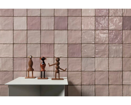 Wandgestaltung mit quadratischen Fliesen und Holzfiguren auf einem Tisch.