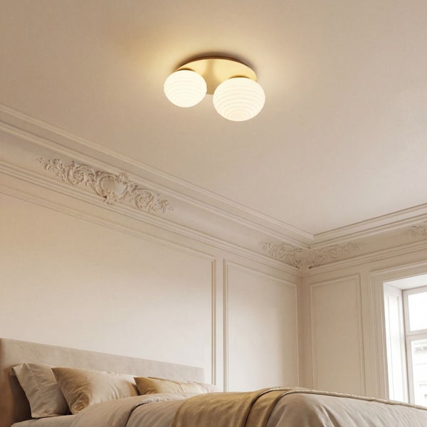 Zweiflammige Deckenleuchte mit weißen Glaskugeln und Messing-Halterung in einem hellen Schlafzimmer mit Stuckverzierungen.