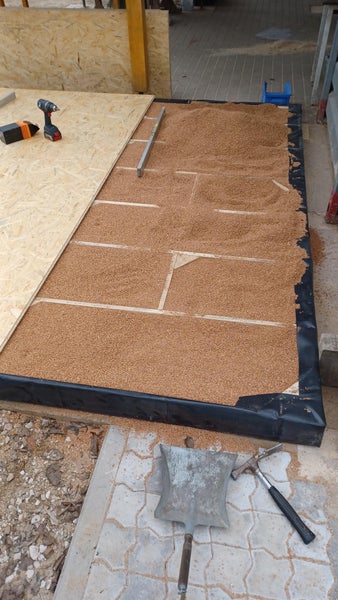 Bau einer Bodenkonstruktion mit Schüttdämmung und OSB Platten auf einer Baustelle mit Werkzeug wie Akkuschrauber und Wasserwaage.