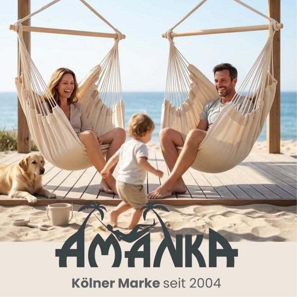 Zwei Personen in beigen AMANKA Hängesesseln auf einer Holzterrasse am Strand mit einem Hund und einem Kind. AMANKA Logo.