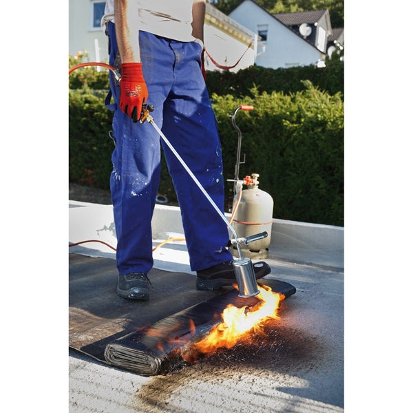 Dachdecker schweißt Bitumenbahn mit einem Gasbrenner auf einem Dach