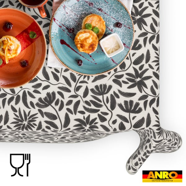 Wachstuch-Tischdecke mit floralem Muster aus Blüten und Blättern, lebensmittelecht, dekorativ gedeckter Tisch mit Tellern und Speisen, ANRO Logo.