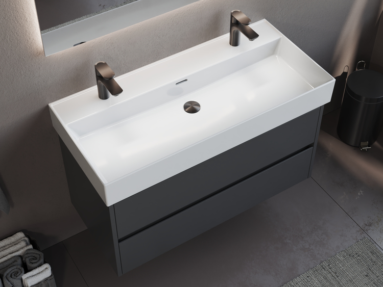 Moderner Doppelwaschtisch mit weißem Becken, zwei dunklen Armaturen und anthrazitfarbenem Unterschrank mit zwei Schubladen.