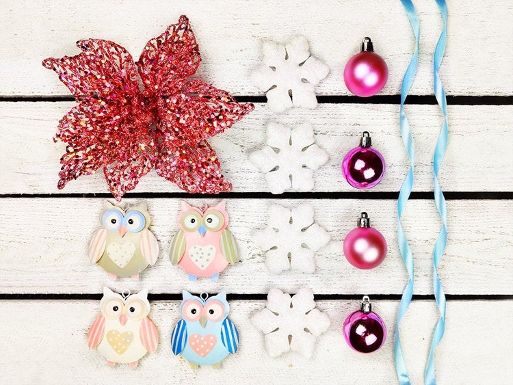Set mit Weihnachtsbaumschmuck aus Eulenfiguren, Schneeflocken, einer künstlichen Blume und Weihnachtskugeln auf weißem Holzuntergrund.