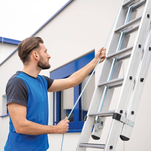 Mann bedient eine Mehrzweckleiter mit Seilzug vor einer Hauswand