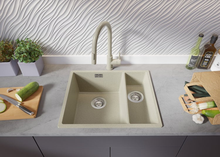 Küchenspüle mit Abtropffläche, Armatur, Schneidebrett mit Zucchini und Einkaufstüte mit Gemüse auf einer Küchentheke.