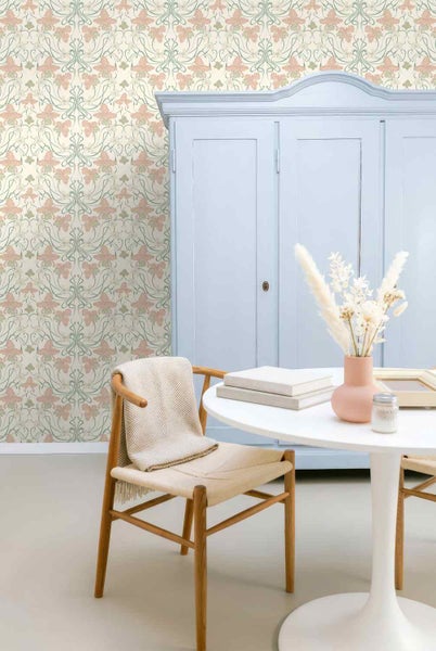 Helle Raumszene mit floraler Tapete im Jugendstil, einem Schrank, einem runden Tisch und einem Holzstuhl.