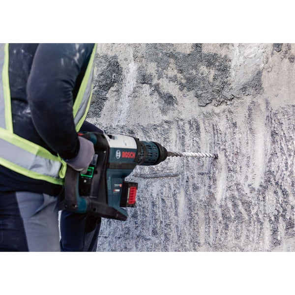 Ein Mann bohrt mit einem Bohrhammer ein Loch in eine Betonwand, wobei der Bosch Logo sichtbar ist.