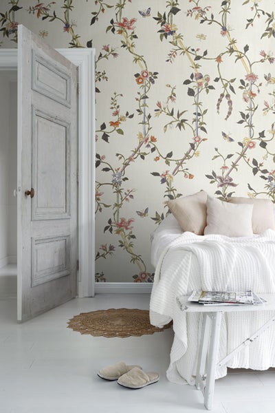 Einladendes Schlafzimmer mit blumiger Tapete, offenstehender Tür und Tagesdecke