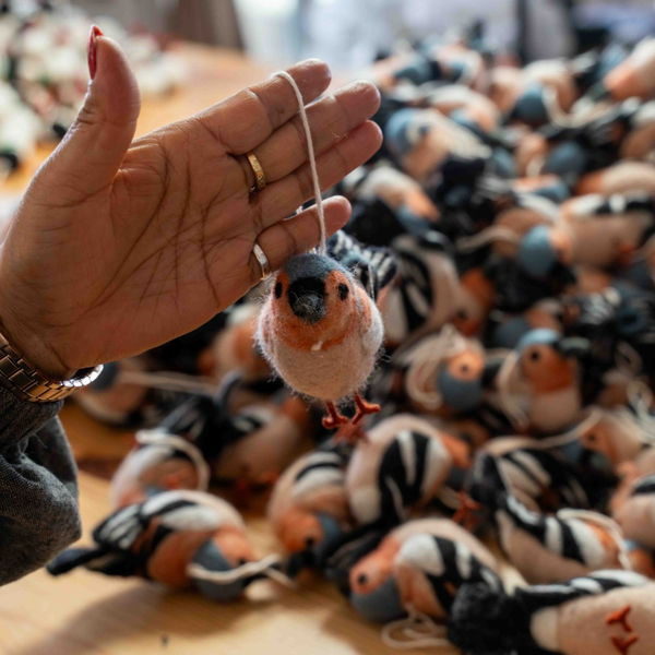 Hand hält eine Vogel-Dekofigur am Faden über einer Menge weiterer Figuren