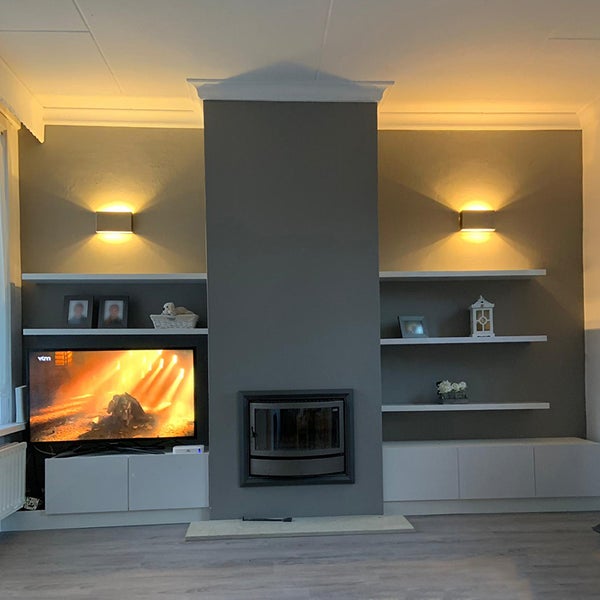 Wohnzimmer mit Kamin, Fernseher, Regalen und Wandleuchten