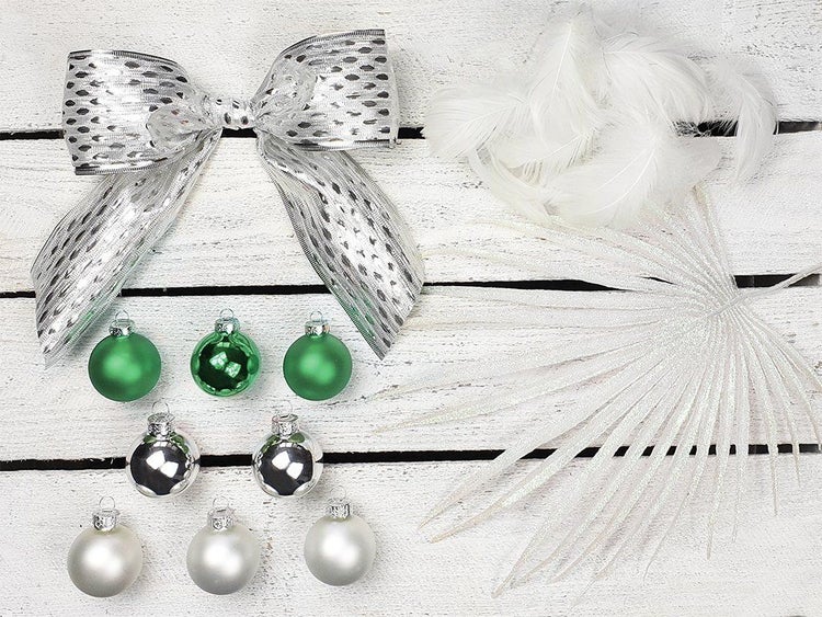 Weihnachtsbaumschmuck Set mit kleinen Kugeln, dekorativer Schleife, Federn und künstlichem Blattzweig auf einem Holzuntergrund.