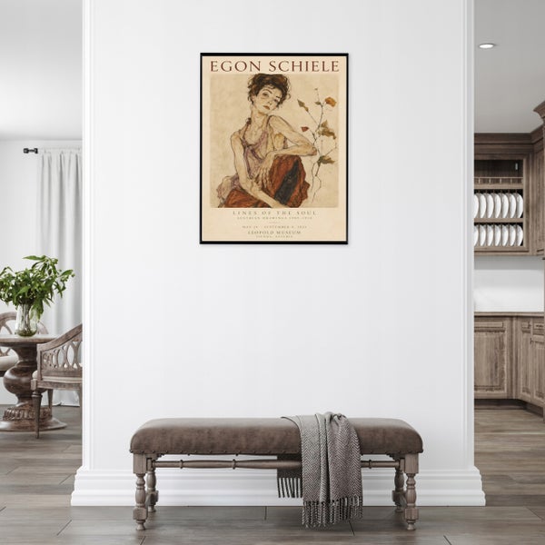 Gerahmtes Kunstdruck Plakat von Egon Schiele an einer weißen Wand mit einer Sitzbank im Vordergrund.