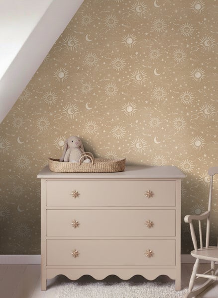 Vliestapete mit Sonnen-, Mond- und Sternenmuster in einem Kinderzimmer mit heller Kommode und Stoffhase.