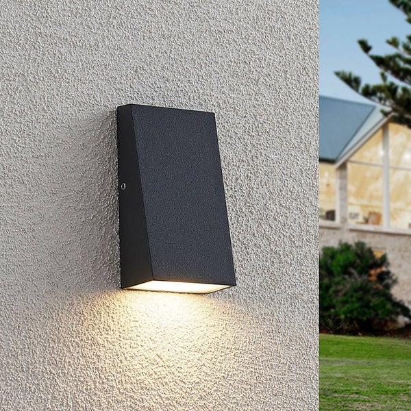 Schwarze, rechteckige Außenwandleuchte an einer weißen Putzfassade mit nach unten gerichtetem Lichtkegel.