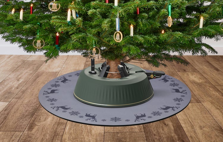 Krinner Christbaumständer auf einer grauen Bodenschutzmatte mit Rentier- und Schneeflockenmuster unter einem geschmückten Weihnachtsbaum.