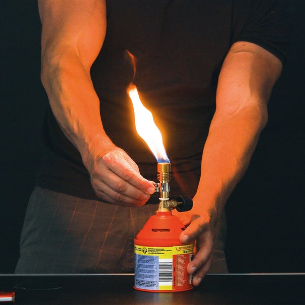 Person zündet Lötlampe auf Tisch an.