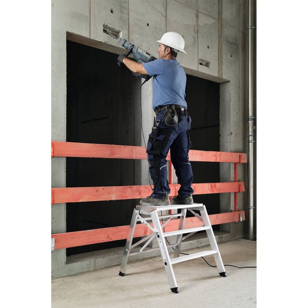 Handwerker arbeitet mit einem Bohrhammer auf einer Trittleiter auf einer Baustelle.