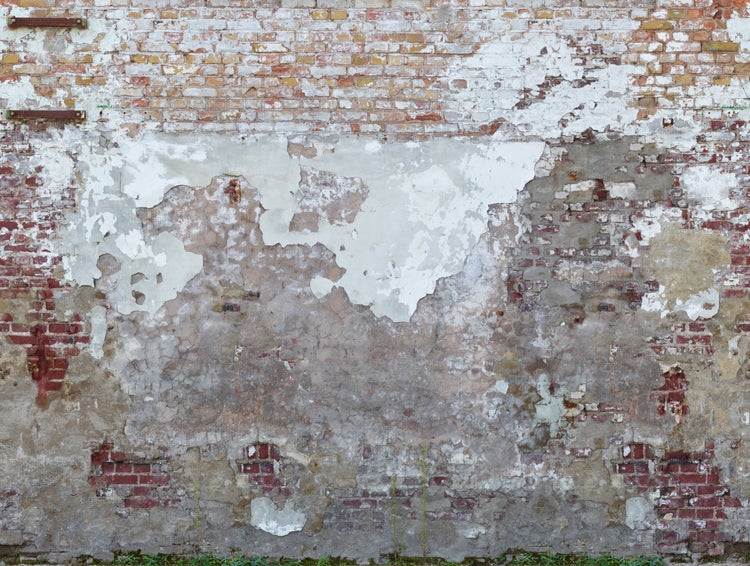 Beschädigte Ziegelwand mit abgeblättertem Putz und Roststellen.